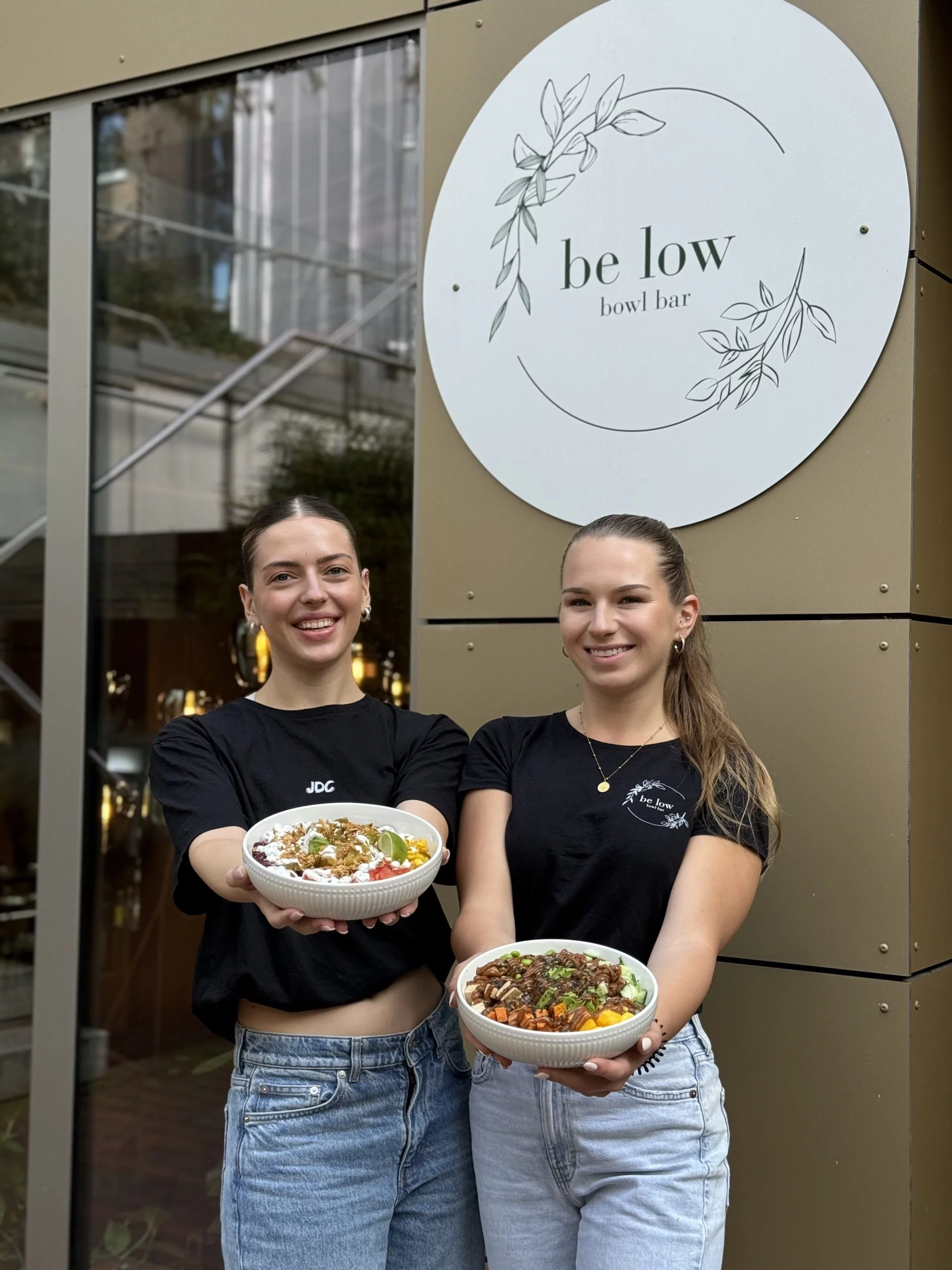Zwei be low Mitarbeiterinnen vor dem be low Logo-Schild am Standort